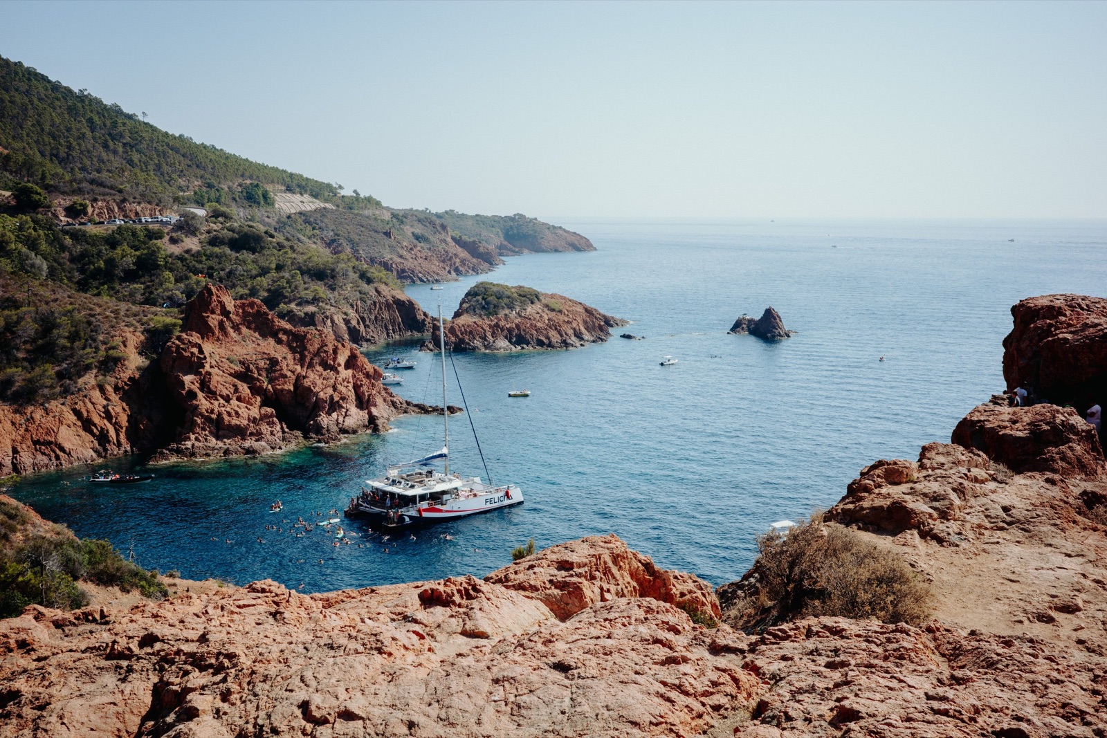 Catamaran anchored with swimmers in a turquoise cove framed by red volcanic rocks