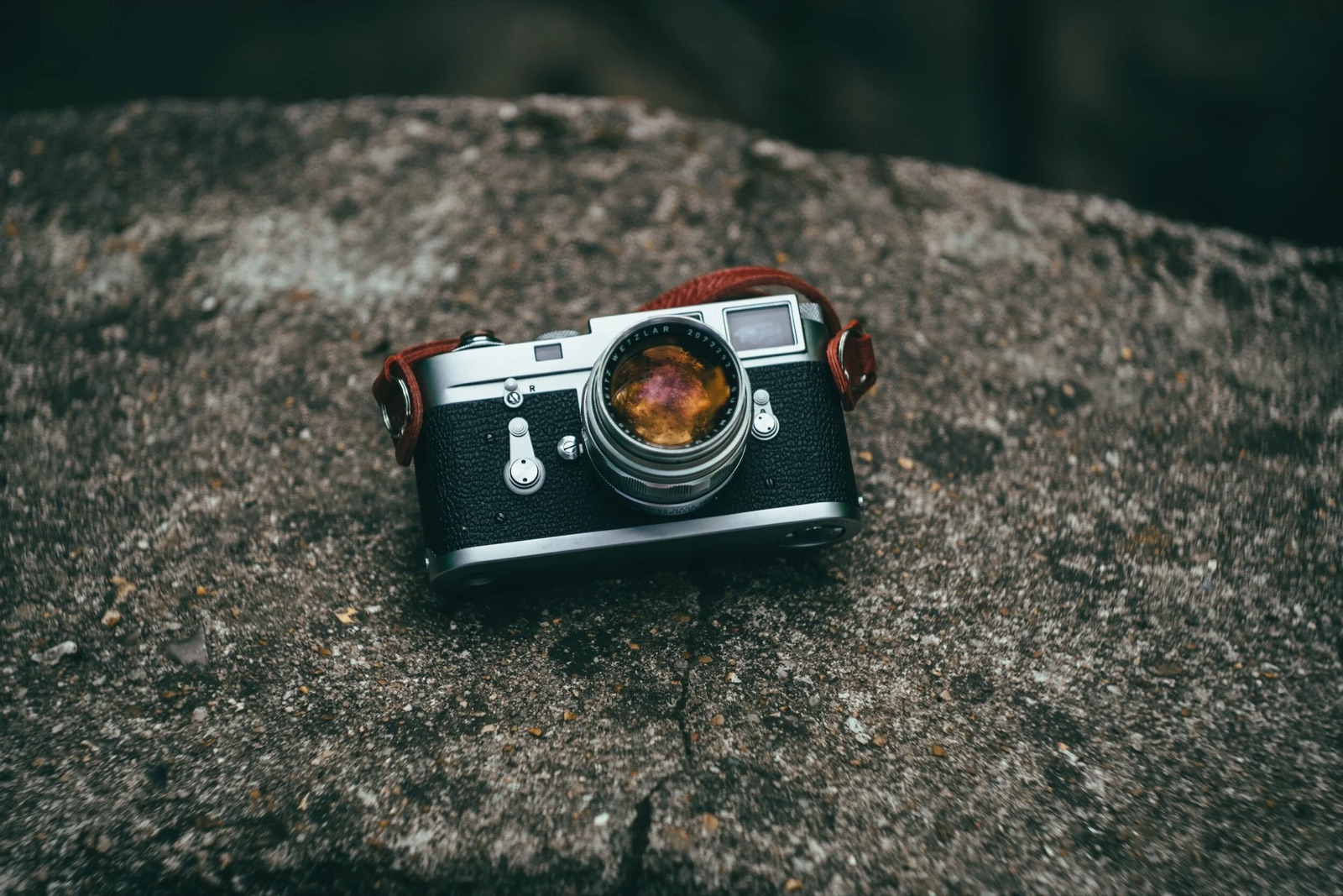 Chrome-and-black rangefinder camera with a red leather strap resting on a concrete slab