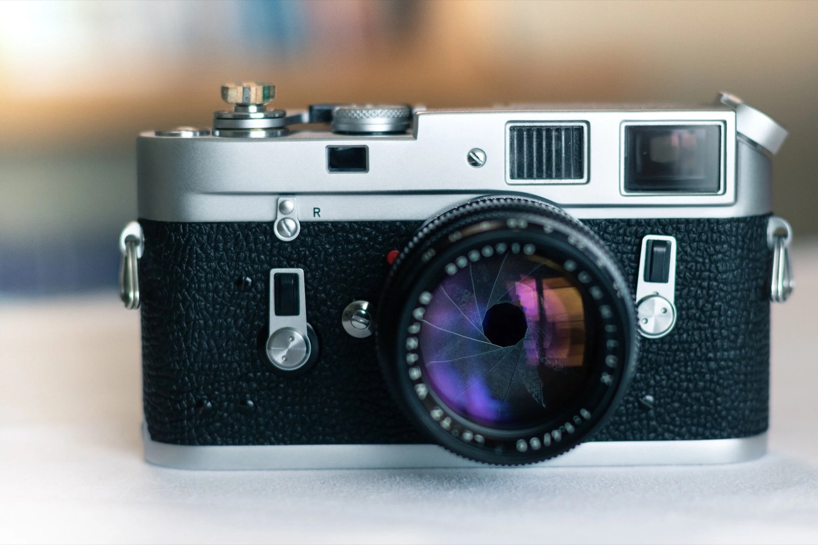 Chrome-top rangefinder camera with a fast lens, aperture blades visible, on a pale surface