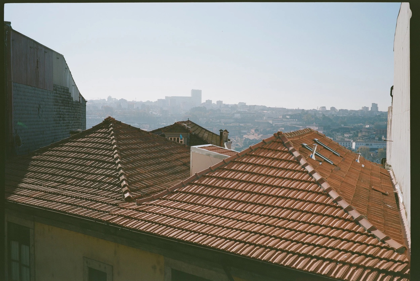Terracotta tiled rooftops stepping down a hillside toward a hazy city skyline
