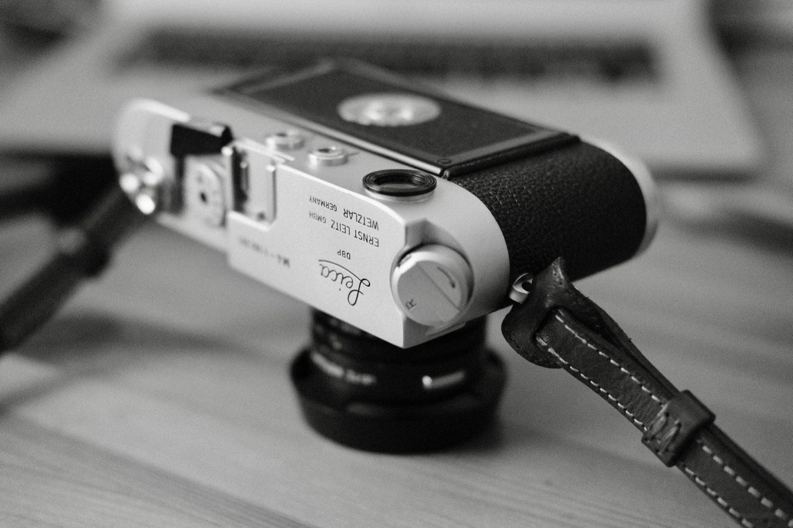Rangefinder camera lying upside down on a wooden table, leather strap coiled beside it