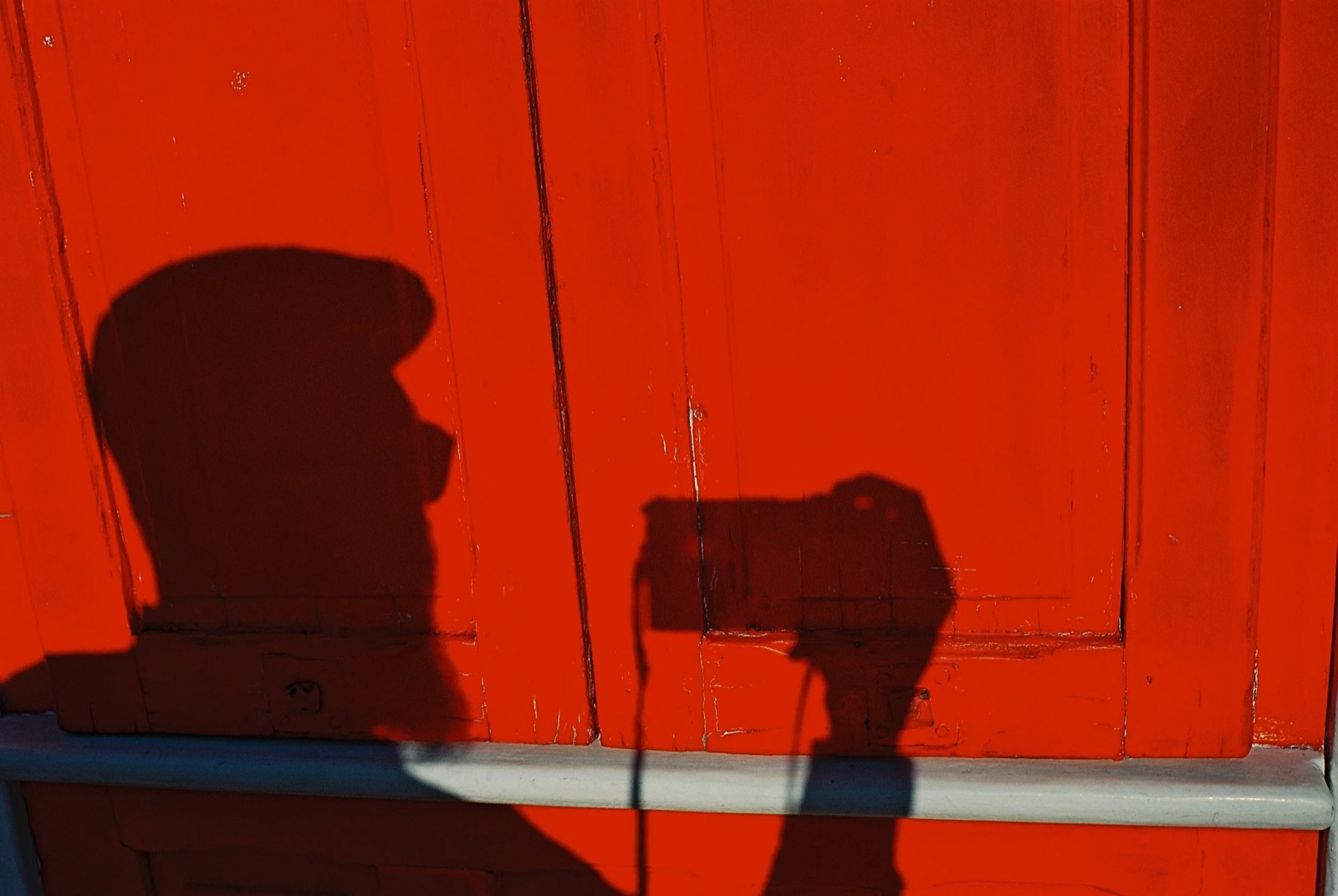 Shadow of a photographer holding a camera cast onto a bright red-painted wooden door