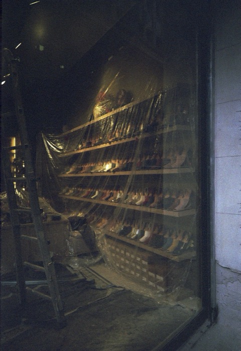 Shoe shop window under renovation, shelves of boots behind plastic sheeting and a ladder