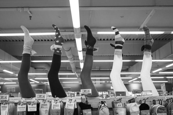 Five mannequin legs in patterned socks stand upright above a supermarket rack of packaged socks