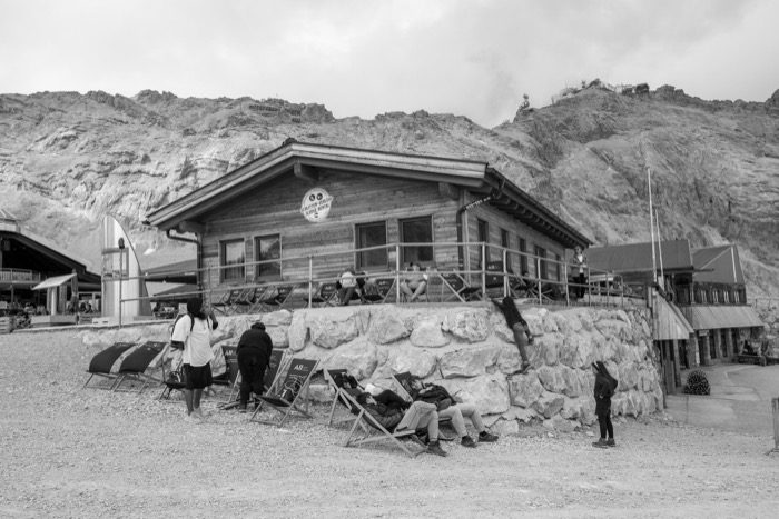 Visitors on deckchairs outside a timber mountain lodge below bare rocky slopes
