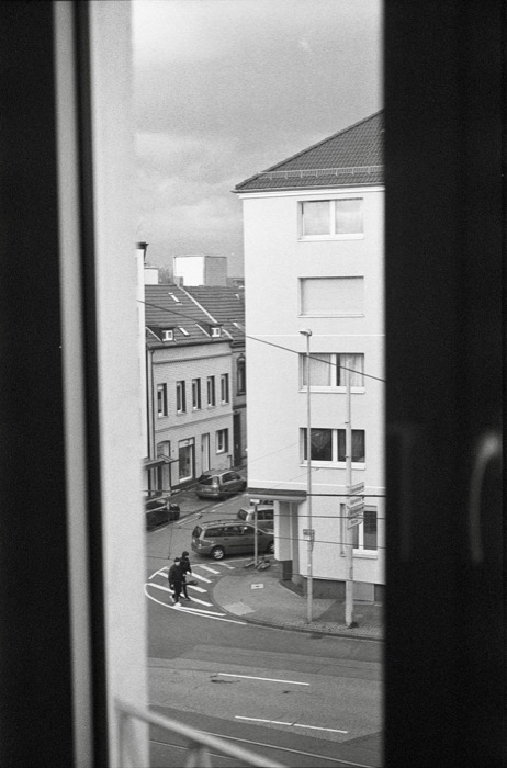 Street corner seen through a gap in a window frame, two figures crossing at the zebra stripes