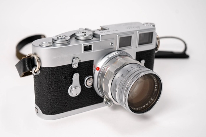 Chrome rangefinder camera with a leather strap resting on a plain white surface