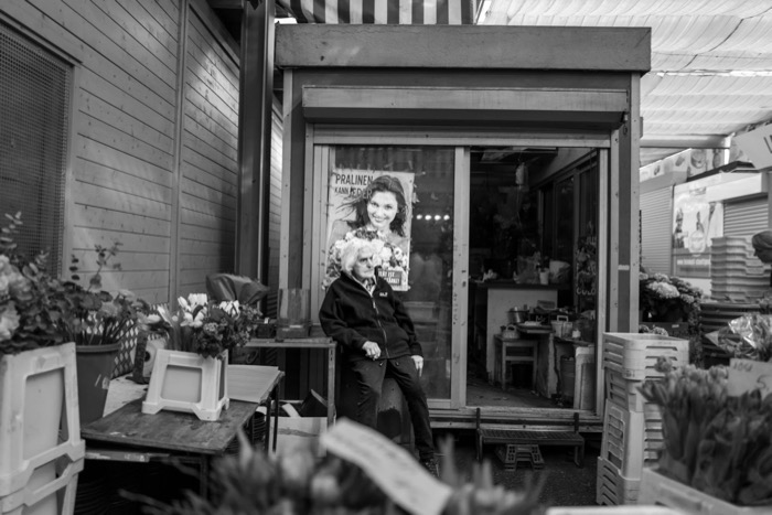 Elderly florist sitting in the doorway of her shop surrounded by buckets of cut flowers