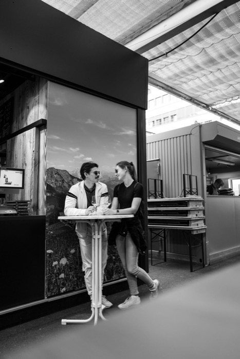 Couple leaning close over a small standing table with wine glasses at a market bar