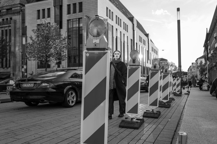 Woman walking a pavement between a line of striped roadworks barriers with lamps on top