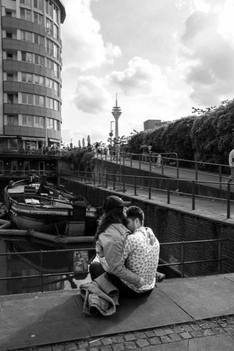 Couple embracing on a harbour quay, a moored barge below and a slender tower beyond