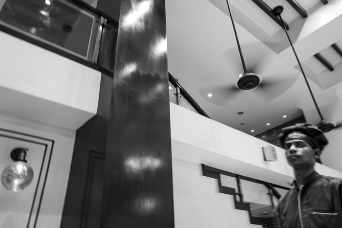 Young man in a cap glancing up in a bright hotel lobby, ceiling fan and polished pillar filling the frame