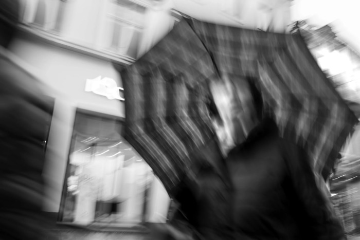 Swirled motion blur of a person under a striped umbrella passing a lit shopfront at night