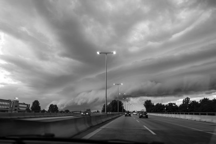 Motorway seen through a windscreen as a huge shelf cloud rolls in above the lit lamp posts