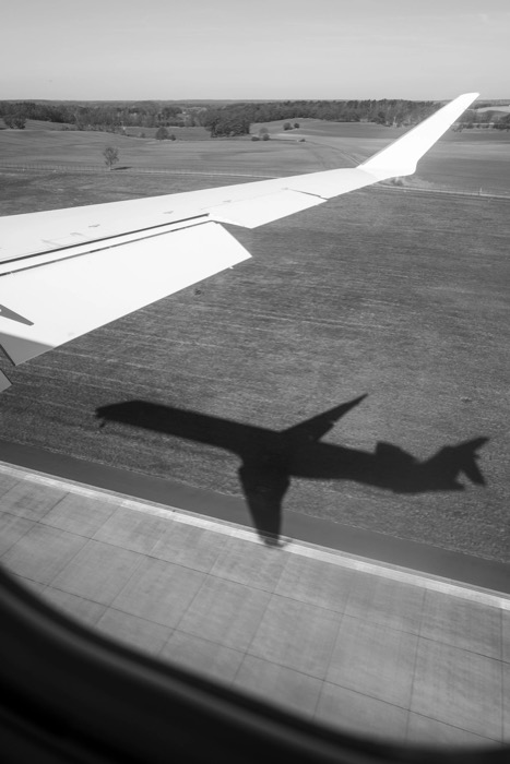 Airliner's shadow cast across fields and runway, seen past the wing from a cabin window