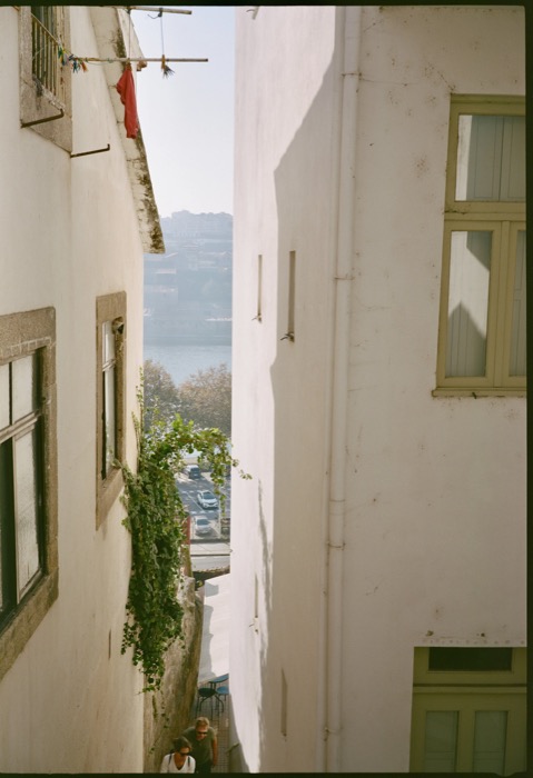 Narrow gap between two whitewashed houses opening onto a hazy river and hillside below