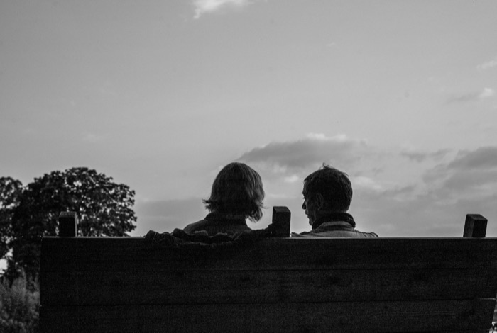 Two people seen from behind above a wooden fence, heads silhouetted against a wide evening sky