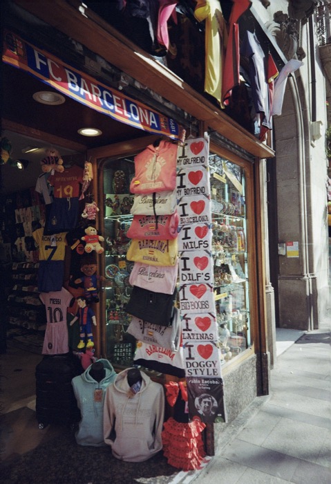 Souvenir shop corner hung with FC Barcelona scarves, football shirts and rows of novelty slogan T-shirts