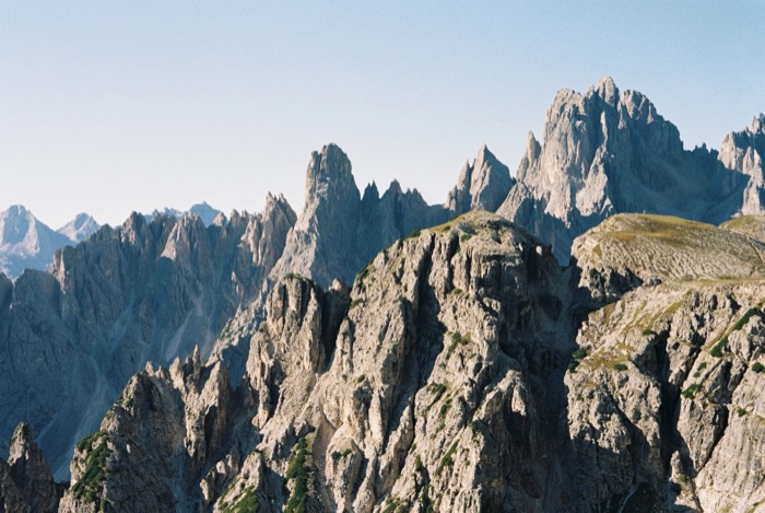 Row of sharp grey limestone spires and scree slopes under a clear pale sky
