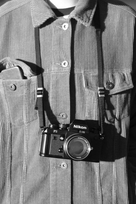 Nikon F3 with 50mm lens hanging on a strap against a corduroy jacket in hard sunlight