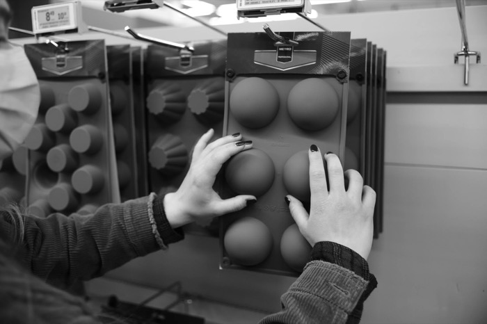 Two hands with dark nail polish pressing into a domed silicone baking mould on a shop display rack