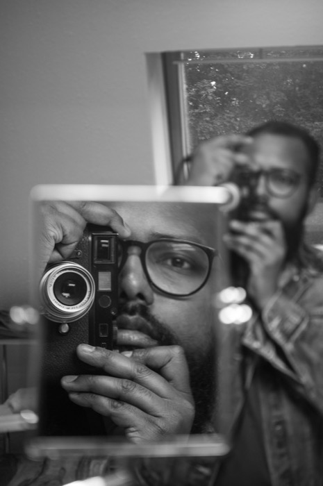 Bearded man in glasses photographing himself twice over in a mirror and a propped frame