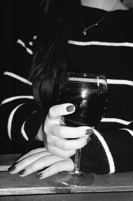 Close view of a woman's hands cradling a glass of wine on a table, striped knit sweater behind