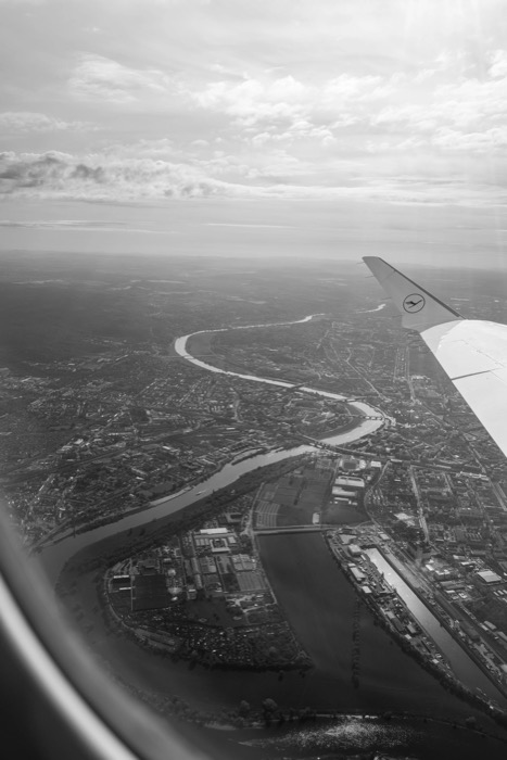 View from an aeroplane window over a city split by a winding river, wingtip in the frame