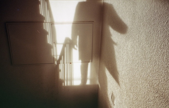 Long shadow of a person cast on a textured stairwell wall beside sunlit banister rails