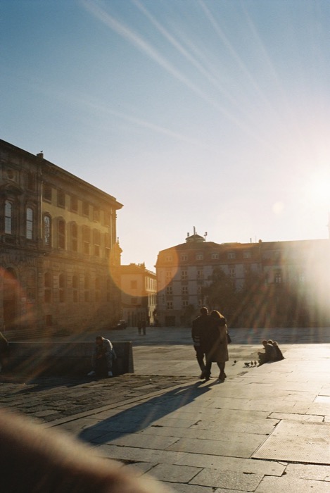Couple walking across a stone plaza into low sun, long shadows and lens flare streaking the frame