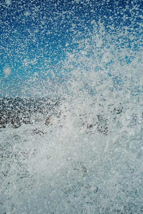 Wall of white spray and foam thrown up against a deep blue sky as a wave breaks
