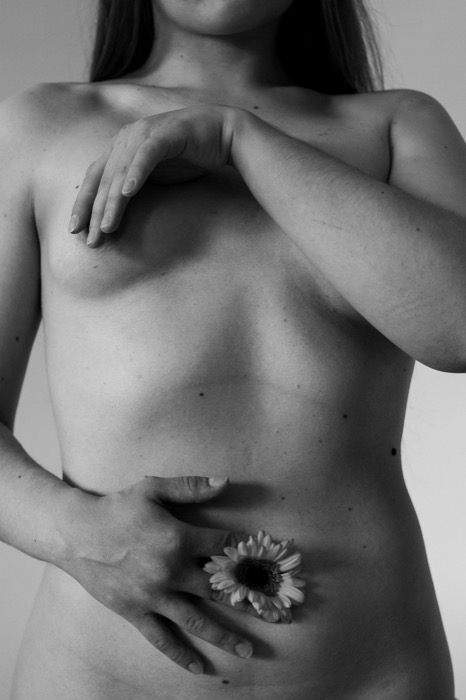 Nude torso with arms crossed over the chest and a single daisy held against the hip