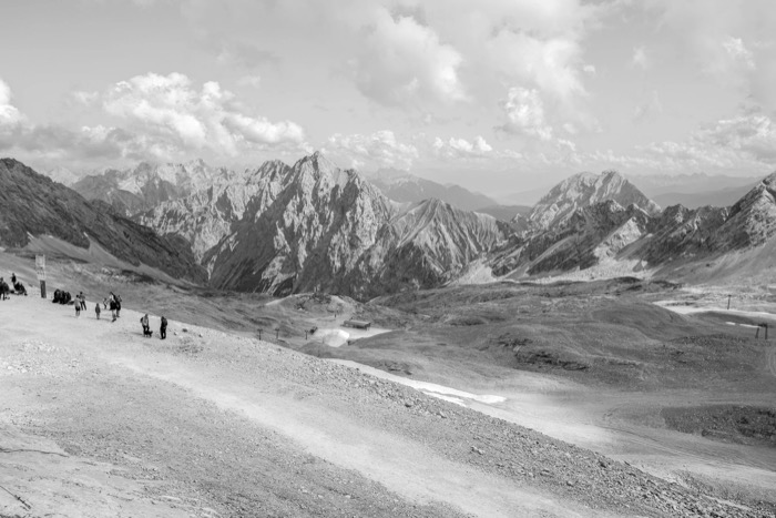 Walkers on a bare high-alpine ridge with rows of rocky peaks stretching to the horizon