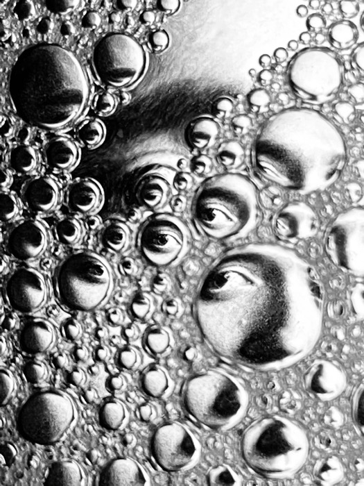 A face repeated and distorted inside a mass of soap bubbles filling the frame