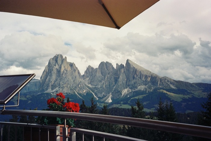 Jagged Dolomite peaks seen from a terrace under a parasol, red geraniums on the railing