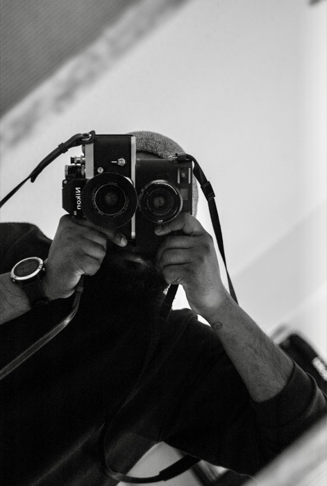 Mirror self-portrait: a bearded man in a beanie holding two film cameras up to his face