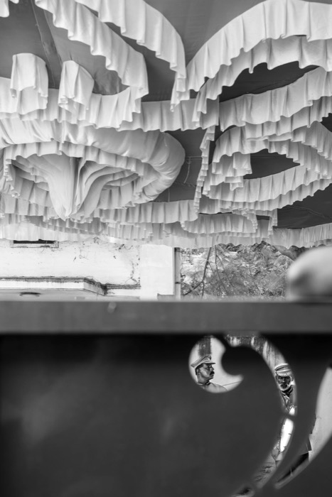 Rows of white cloth hung to dry overhead, with two uniformed figures glimpsed through a gap below