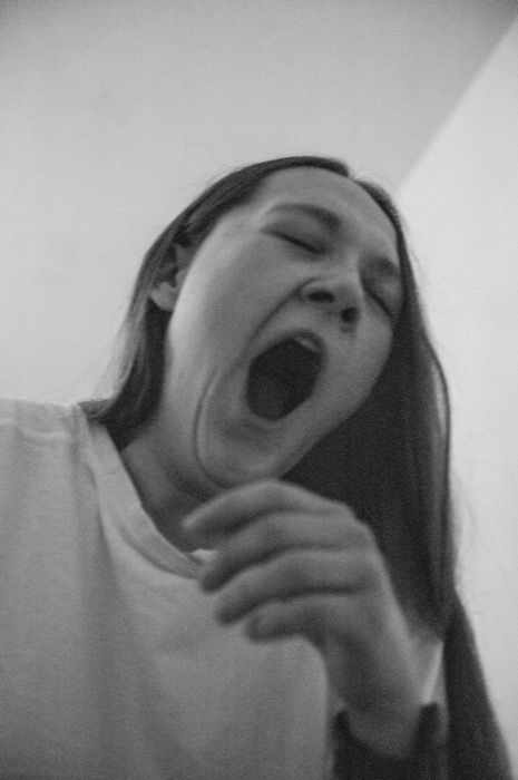Long-haired woman yawning wide, shot from below against a plain wall