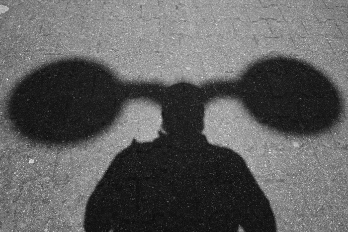 Shadow of a person on pavement with two huge round shapes flanking the head like ears