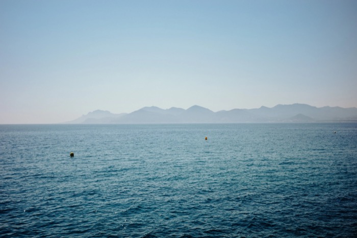 Calm blue sea stretching to a hazy mountain coastline, two small buoys breaking the surface