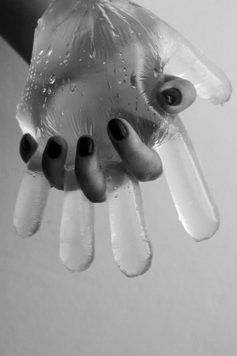 Hand with dark nail polish inside a water-beaded latex glove, the empty fingers hanging limp