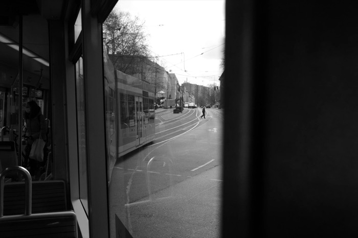 View from inside a tram through reflecting glass to an empty street where one person crosses the tracks