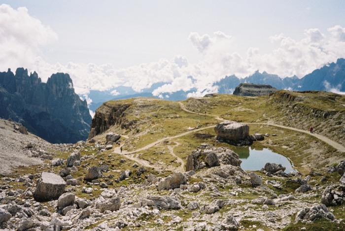 Rocky mountain plateau with a small tarn, footpaths and distant spires above a sea of cloud