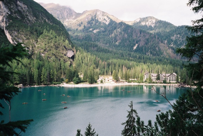 Turquoise mountain lake dotted with rowing boats, forested slopes and a lakeside hotel beyond