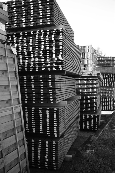 Towering stacks of labelled timber boards in a yard, receding in repeating layers against a white sky