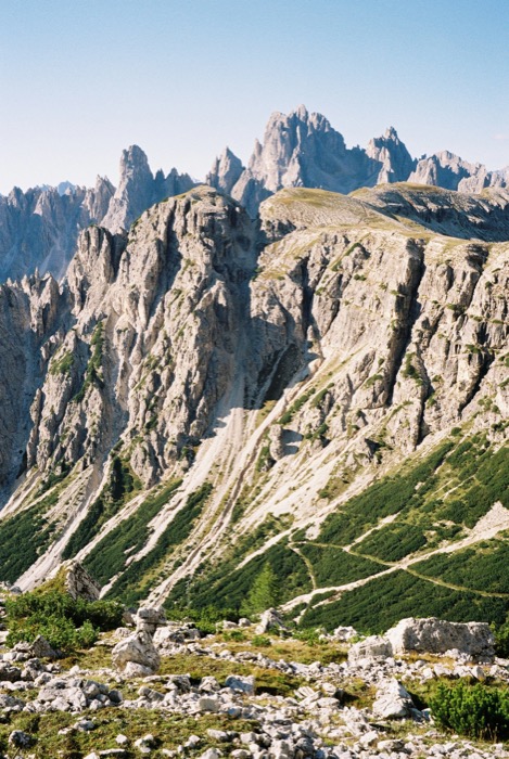 Hiking path threading a boulder-strewn meadow beneath fluted grey mountain walls and pinnacles