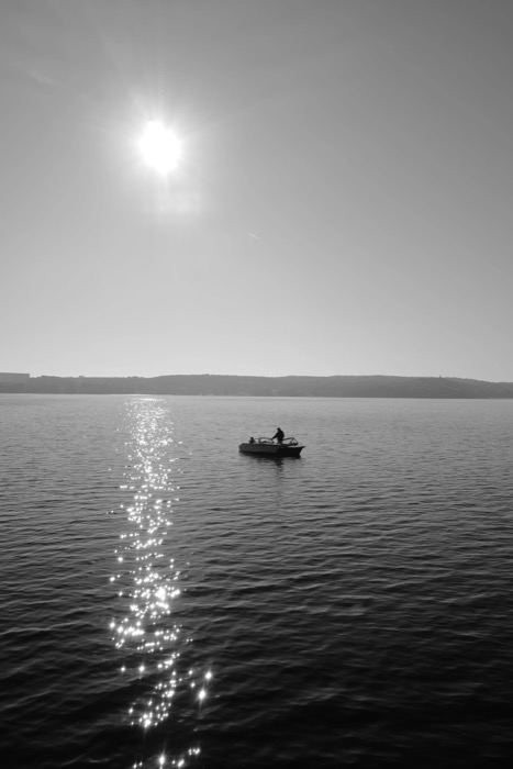 Small motorboat silhouetted on open water beneath a low sun and its glittering path