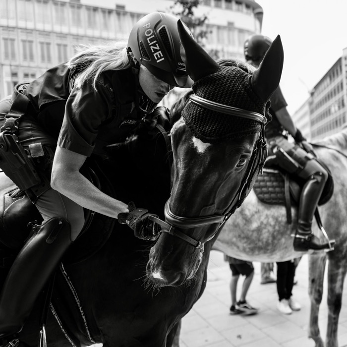 Mounted police officer in a Polizei helmet leaning down to adjust her horse's bridle