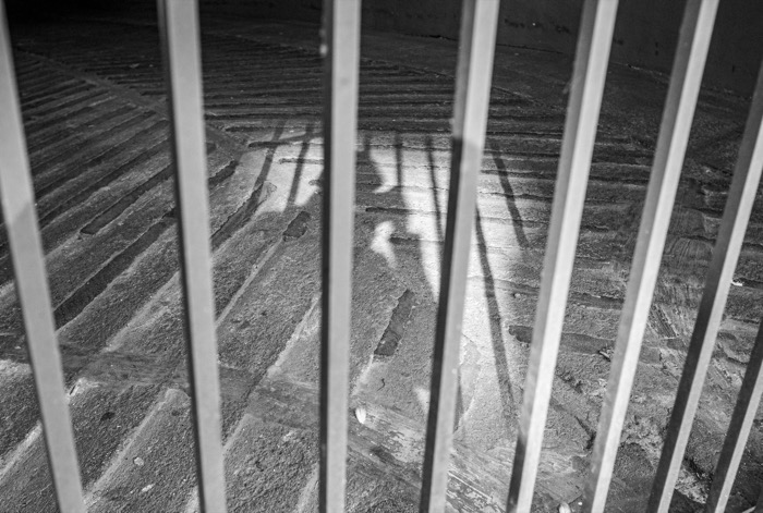 Shadow of a person cast on herringbone brick paving, seen through the vertical bars of a railing