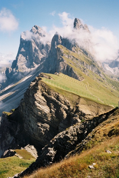 Grassy ridge falling away below jagged limestone peaks wrapped in cloud